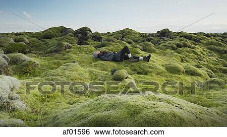 Side view of woman laying in mossy field in remote rocky landscape under clear blue sky View Large Photo Image Stock Photograph - Side view of woman laying in mossy field in remote rocky landscape under clear blue sky. Fotosearch