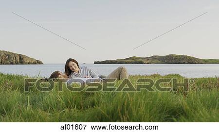 Smiling boyfriend and girlfriend laying in grassy field near lake in remote landscape under blue sky View Large Photo Image Stock Photo - Smiling boyfriend and girlfriend laying in grassy field near lake in remote landscape under blue sky. Fotosearch