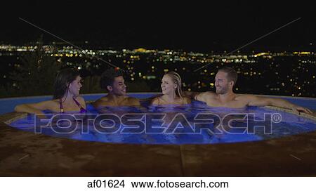 Smiling couples sitting in illuminated hot tub overlooking cityscape at night View Large Photo Image Picture - Smiling couples sitting in illuminated hot tub overlooking cityscape at night. Fotosearch