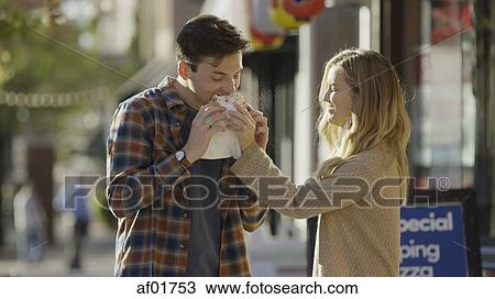 Smiling girlfriend feeding boyfriend sandwich outside store View Large Photo Image Stock Image - Smiling girlfriend feeding boyfriend sandwich outside store. Fotosearch