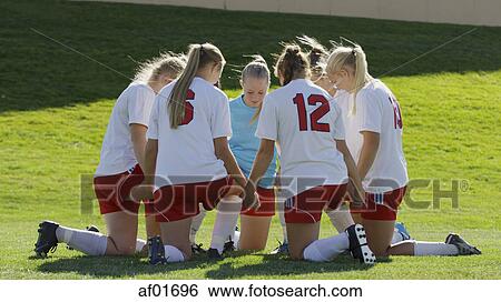 Stock Photograph - Soccer team players kneeling and holding hands in huddle before game. Fotosearch