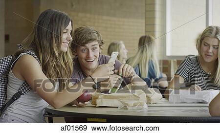 Stock Photo - Students eating lunch and using cell phone during recess in school cafeteria. Fotosearch