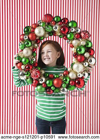 Stock Image - Studio portrait of girl (4-5) holding Christmas decoration. Fotosearch