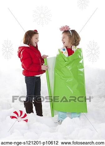 Stock Image - Studio shot of girl (4-5) wrapping friend (6-7) as Christmas gifts. Fotosearch