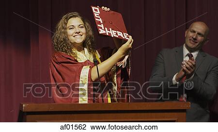 Teacher applauding smiling student holding decorated mortarboard hat at podium on stage during graduation ceremony View Large Photo Image Stock Image - Teacher applauding smiling student holding decorated mortarboard hat at podium on stage during graduation ceremony. Fotosearch