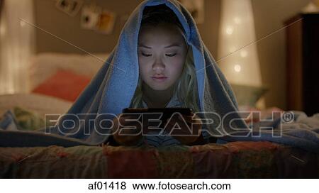 Teenage girl wrapped in blanket using cell phone in bed View Large Photo Image Stock Photo - Teenage girl wrapped in blanket using cell phone in bed. Fotosearch