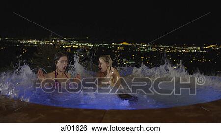 Women splashing in illuminated jacuzzi hot tub overlooking cityscape at night View Large Photo Image Stock Photograph - Women splashing in illuminated jacuzzi hot tub overlooking cityscape at night. Fotosearch
