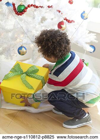 Stock Photography - Young boy picking up Christmas present from under Christmas tree. Fotosearch