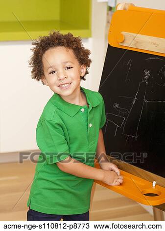 Stock Image - Young boy posing by small blackboard. Fotosearch