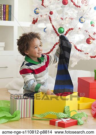 Picture - Young boy sitting under Christmas tree, opening Christmas presents. Fotosearch