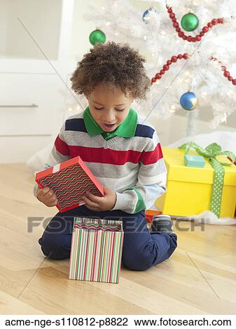 Stock Image - Young boy sitting under Christmas tree, opening Christmas presents. Fotosearch