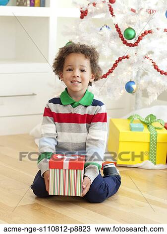 Young boy sitting under Christmas tree, holding Christmas present View Large Photo Image Stock Image - Young boy sitting under Christmas tree, holding Christmas present. Fotosearch