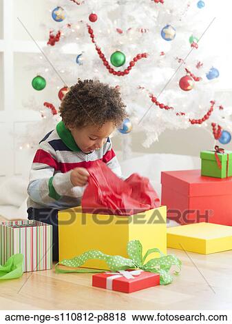 Stock Photo - Young boy sitting under Christmas tree, opening Christmas presents. Fotosearch