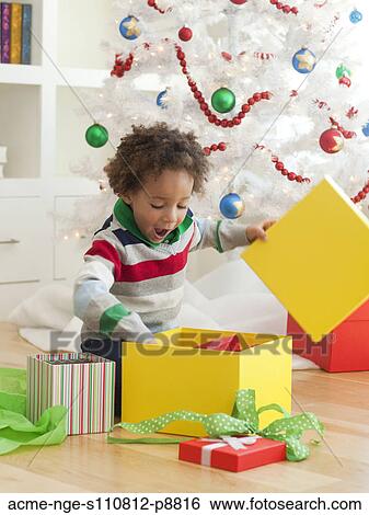Stock Photograph - Young boy sitting under Christmas tree, opening Christmas presents. Fotosearch
