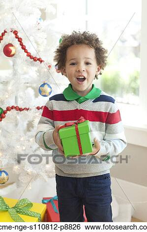 Stock Photograph - Young boy sitting under Christmas tree, holding Christmas present. Fotosearch