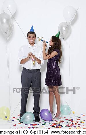 Picture - Young couple blowing horns at party. Fotosearch