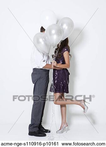 Stock Image - Young couple kissing behind balloons at party. Fotosearch