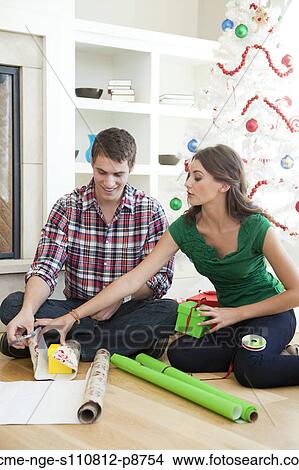 Picture - Young couple sitting on floor, wrapping Christmas presents. Fotosearch