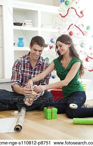 Stock Image - Young couple sitting on floor, wrapping Christmas presents. Fotosearch