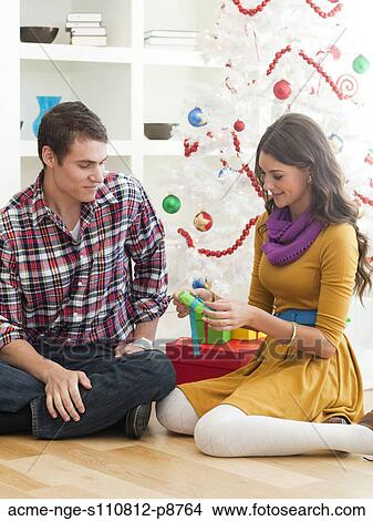 Young couple sitting under Christmas tree, opening Christmas present View Large Photo Image Picture - Young couple sitting under Christmas tree, opening Christmas present. Fotosearch