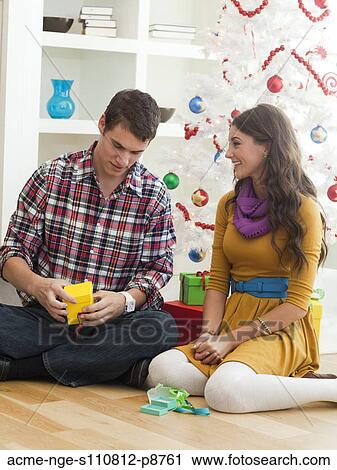 Stock Image - Young couple sitting under Christmas tree. Fotosearch