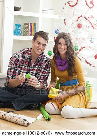 Young couple sitting under Christmas tree, wrapping Christmas presents View Large Photo Image Stock Photo - Young couple sitting under Christmas tree, wrapping Christmas presents. Fotosearch