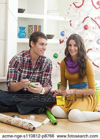 Young couple sitting under Christmas tree, wrapping Christmas presents View Large Photo Image Stock Photograph - Young couple sitting under Christmas tree, wrapping Christmas presents. Fotosearch