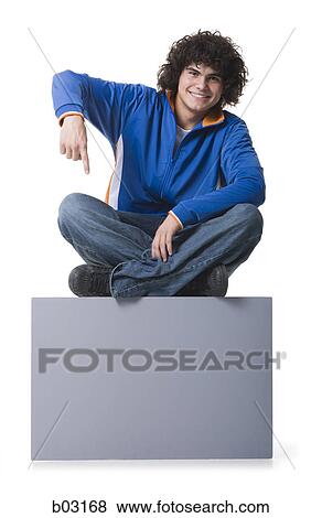 Portrait of a teenage boy sitting on a blank sign and pointing View Large Photo Image Stock Photo - Portrait of a teenage boy sitting on a blank sign and pointing. Fotosearch