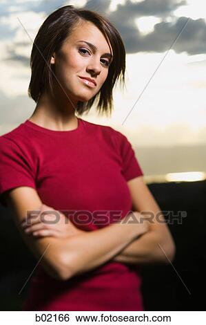 Portrait of a young woman standing with her arms crossed View Large Photo Image Stock Photograph - Portrait of a young woman standing with her arms crossed. Fotosearch