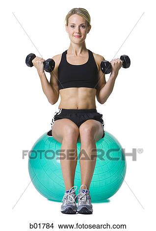 Portrait of a young woman sitting on a fitness ball holding dumbbells View Large Photo Image Picture - Portrait of a young woman sitting on a fitness ball holding dumbbells. Fotosearch