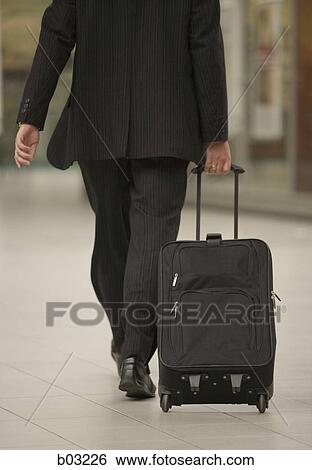 Rear view of a man pulling a suitcase View Large Photo Image Stock Photograph - Rear view of a man pulling a suitcase. Fotosearch