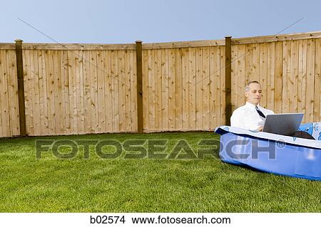 Picture - Businessman working on a laptop, sitting in a wading pool. Fotosearch