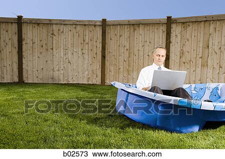 Stock Image - Mid adult man working on a laptop sitting in a wading pool. Fotosearch