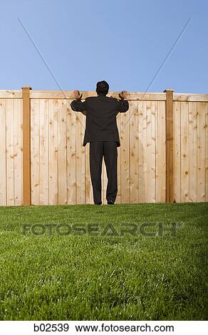Rear view of a businessman standing in front of a fence View Large Photo Image Stock Photo - Rear view of a businessman standing in front of a fence. Fotosearch