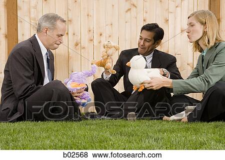 Two businessmen and a businesswoman playing with toys sitting on a lawn View Large Photo Image Stock Photo - Two businessmen and a businesswoman playing with toys sitting on a lawn. Fotosearch