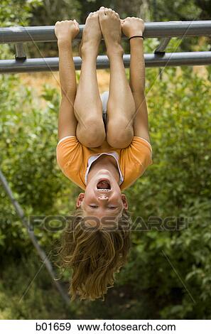 Stock Photo - Girl hanging upside down from a jungle gym. Fotosearch
