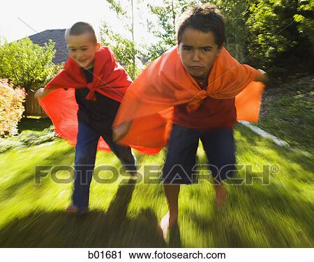 Stock Image - Low angle view of two boys wearing capes and running. Fotosearch
