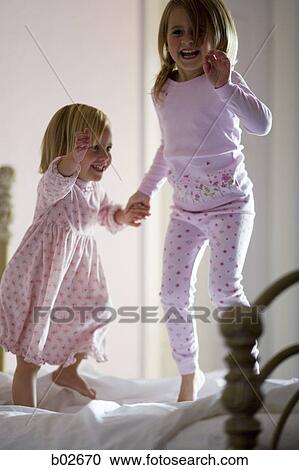Stock Image - Two girls jumping on the bed. Fotosearch