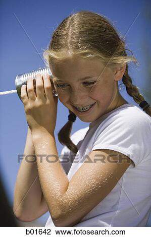 Low angle view of a girl listening into a tin can phone View Large Photo Image Stock Image - Low angle view of a girl listening into a tin can phone. Fotosearch