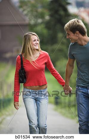 Picture - Teenage couple holding hands and walking together on a path. Fotosearch