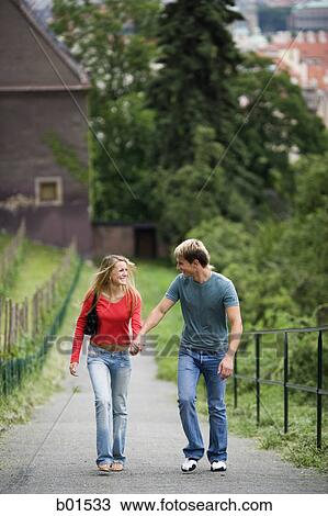 Teenage couple holding hands and walking together on a path View Large Photo Image Stock Image - Teenage couple holding hands and walking together on a path. Fotosearch