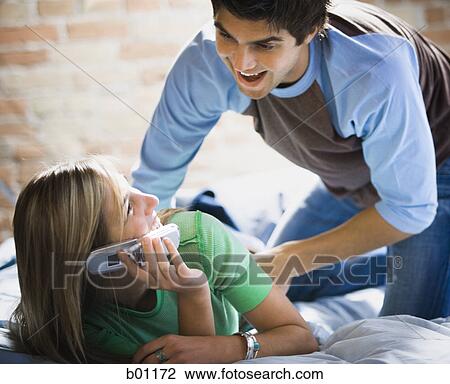 Stock Image - Young man bending over a young woman lying on a bed. Fotosearch