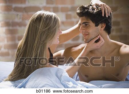 Stock Photograph - Close-up of young woman and man looking at each other on a bed. Fotosearch