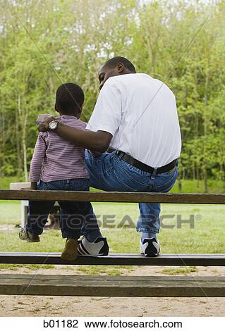 Father and son sitting on a park bench View Large Photo Image Stock Image - Father and son sitting on a park bench. Fotosearch