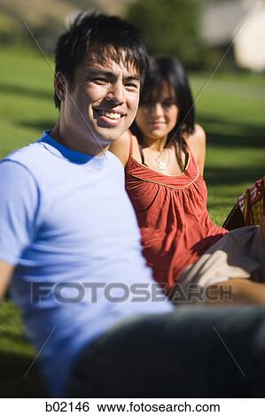 Close-up of a young couple sitting in a park View Large Photo Image Stock Photograph - Close-up of a young couple sitting in a park. Fotosearch
