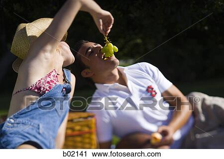 Stock Image - Close-up of a young woman feeding grapes to a young man. Fotosearch