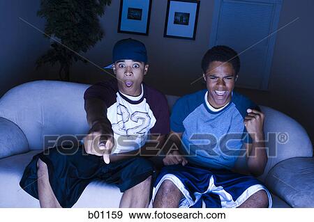 High angle view of a young man and a teenage boy sitting on a couch watching television View Large Photo Image Stock Photo - High angle view of a young man and a teenage boy sitting on a couch watching television. Fotosearch