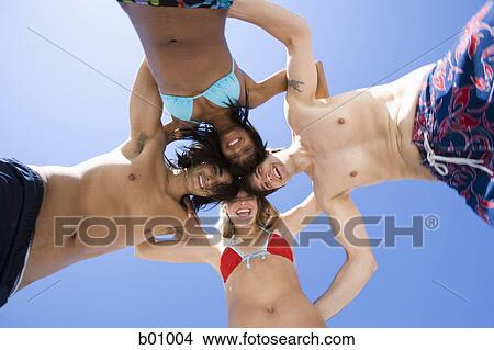 Picture - Low angle view of four young people in a huddle on the beach. Fotosearch