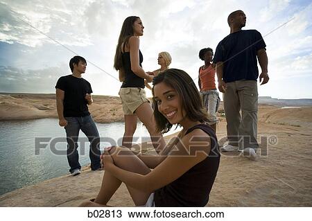 Stock Image - Portrait of a young woman sitting on a rock with friends in the background. Fotosearch