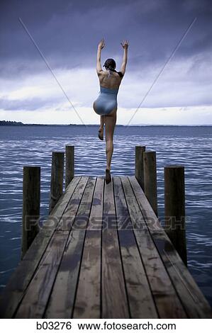 Stock Photograph - Rear view of a young woman jumping from a pier. Fotosearch
